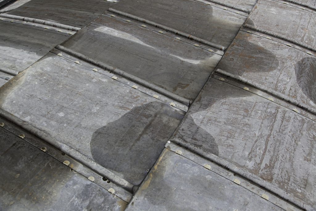 Old weathered metal roof with standing water, showing vulnerability before Roof Inspection Western New York.